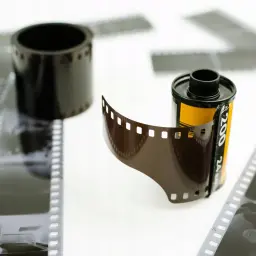 Rolka filmu i wywołanie zdjęć z kliszy. W tle inne klisze i rolka filmu.